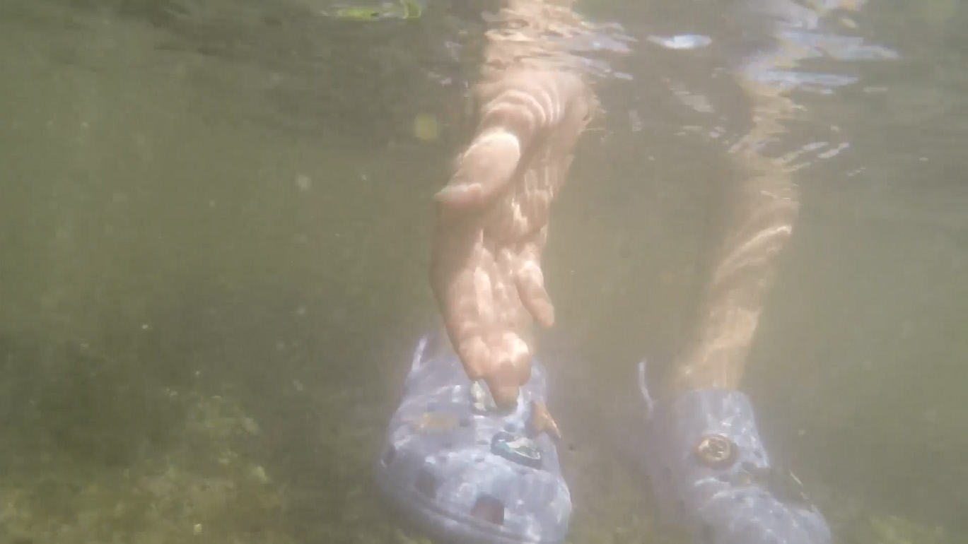 A hand and some croc shoes viewed from under murky stream water