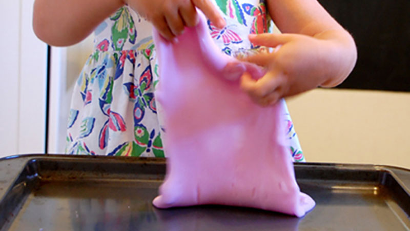 Kid playing with smooshy slime over a baking sheet.