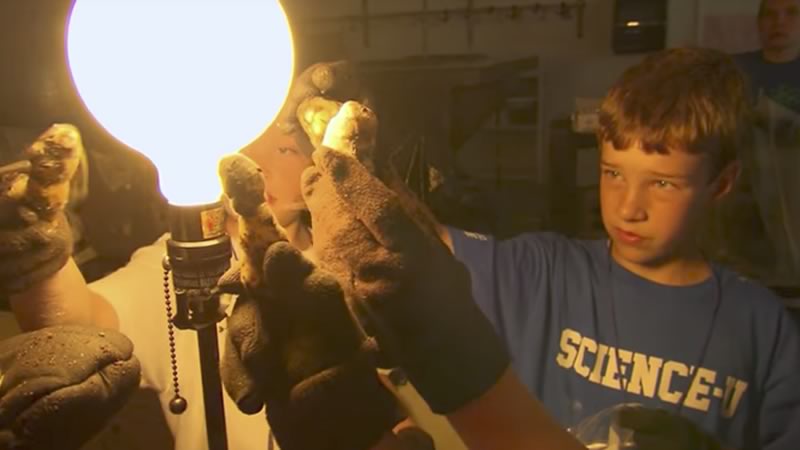 A young scientist holds up a dry ice comet in front of a light bulg.